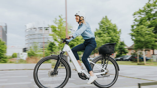 A woman rides her eBike on a street and smiles.