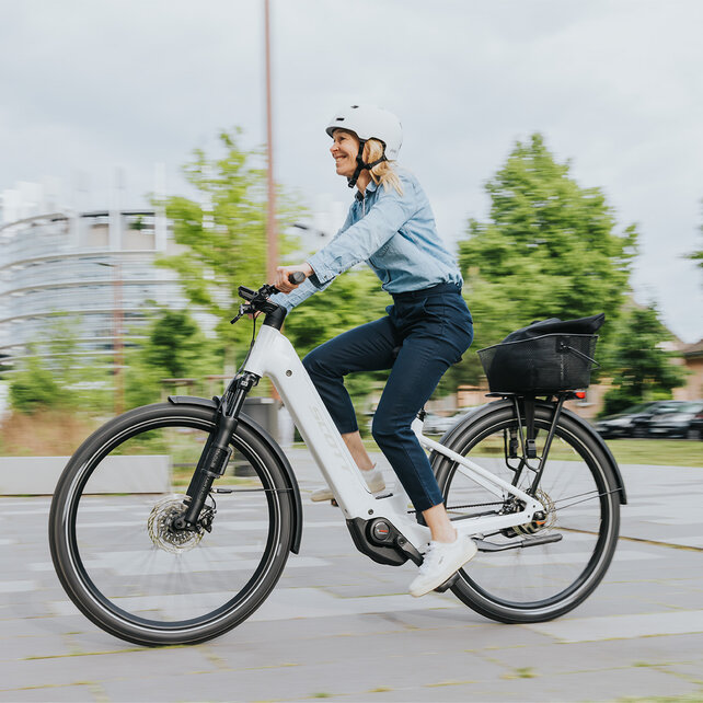 A woman rides her eBike on a street and smiles.