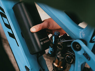 A person is attaching a Bosch PowerMore 250 battery to a blue e-mountain bike.