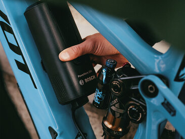 A person is attaching a Bosch PowerMore 250 battery to a blue e-mountain bike.