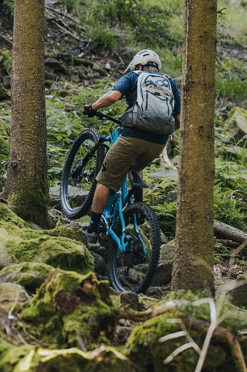 An eMountain biker rides uphill on a narrow trail, surrounded by fir trees and moss-covered rocks in Sasbachwalden.