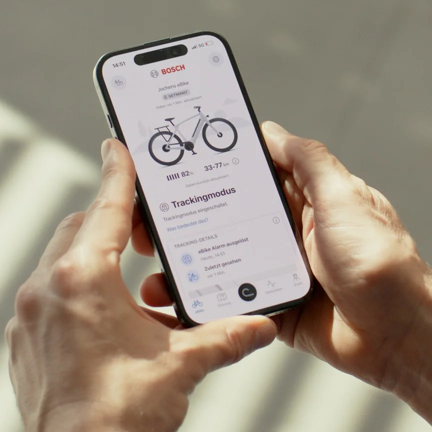 Eine Person hält ein Smartphone mit der geöffneten Bosch eBike Flow App. Der Bildschirm zeigt den aktivierten Trackingmodus und einen ausgelösten eBike-Alarm, eine Funktion des eBike-Diebstahlschutzes.