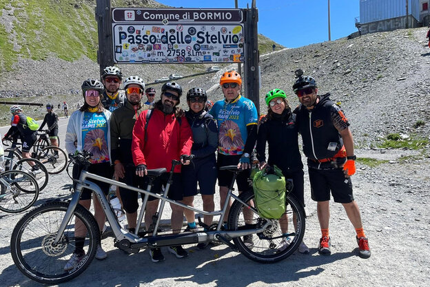 Diversi eBike eBiker posano davanti a un cartello "Passo dello Stelvio" con una bici tandem.