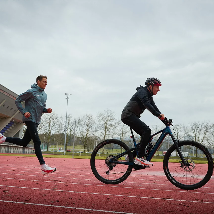 Viktor Röthlin, dans sa fonction d’entraîneur de course à pied, roule devant avec son VAE, tandis que le coureur d’orientation Matthias Kyburz le suit.