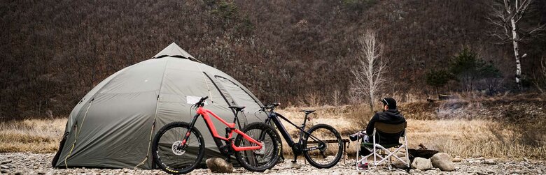 A man is sitting next to the 2 ebikes and a tent