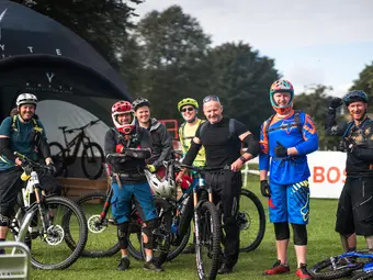 Seven cyclists in full gear are gathered together, smiling happily for a photo.