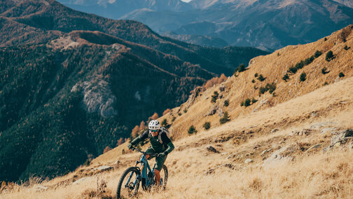 A man is riding an eBike up a steep hill, surrounded by a stunning mountain landscape.