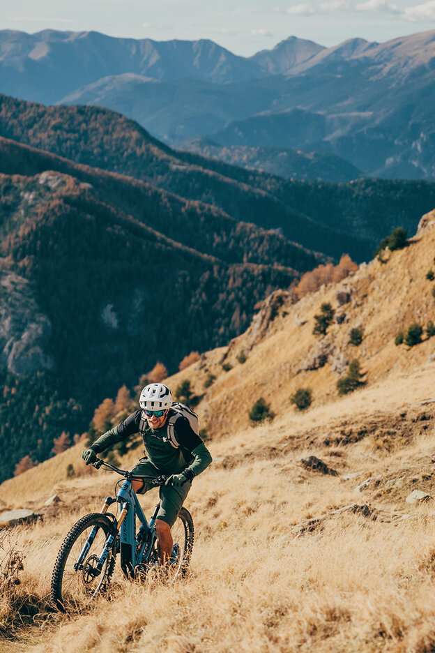 A man is riding an eBike up a steep hill, surrounded by a stunning mountain landscape.
