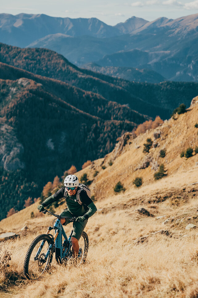 A man is riding an eBike up a steep hill, surrounded by a stunning mountain landscape.