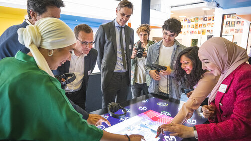 Een groep mensen staat rondom een groot display en gebruikt het interactief.