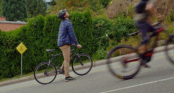 A fatigued cyclist being overtaken by an eBike rider on a hill.