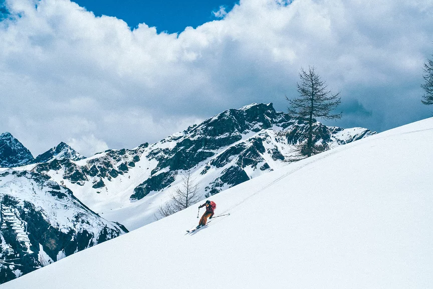 Un skieur descend une montagne enneigée. En arrière-plan, on aperçoit d’autres montagnes.