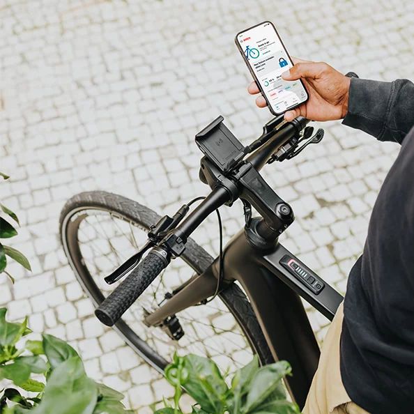 Smartphone wird in der einen Hand gehalten, auf dem die Startseite der eBike Flow App zu sehen ist. Mit der anderen Hand wird der eBike-Lenker gehalten.