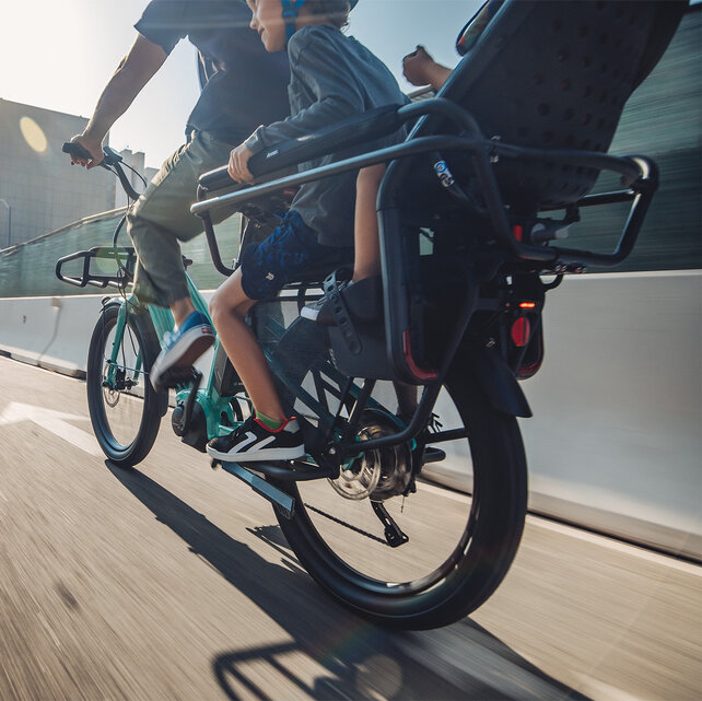 A rider/eBiker is fast driving on a road, while behind him on the eBike two children are riding.