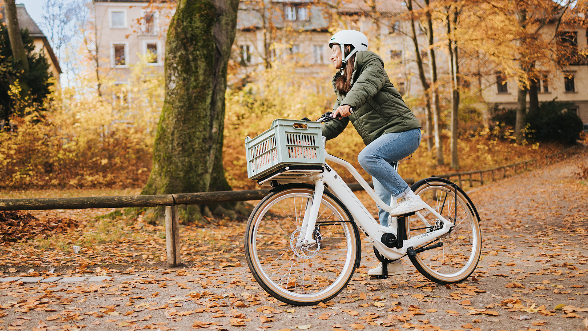 A woman wearing a helmet rides a white eBike in an autumn park.