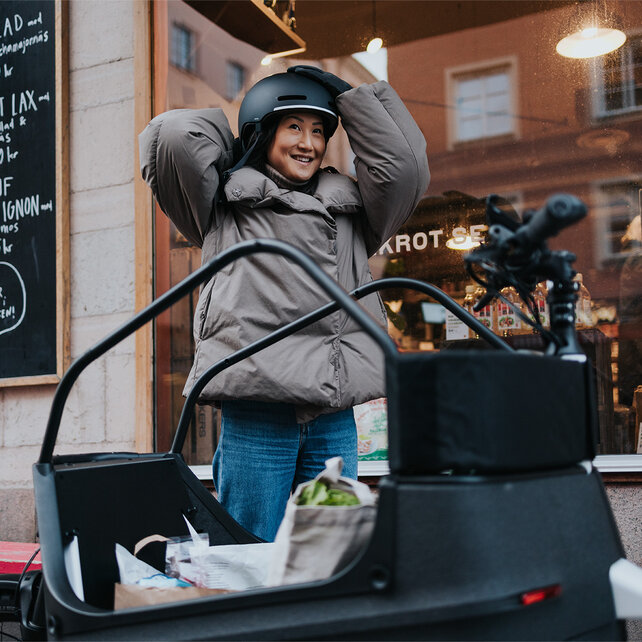 Eine Frau setzt ihren Helm auf. Vor ihr steht ein vollbeladenes eCargo Bike.
