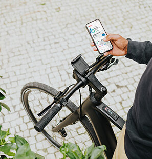Eine Person hält ein Smartphone, auf dem die eBike Flow App geöffnet ist, im Hintergrund ist ein eBike zu sehen.