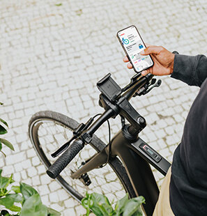 Une personne tient un smartphone sur lequel l'application eBike Flow est ouverte, avec un vélo électrique en arrière-plan.