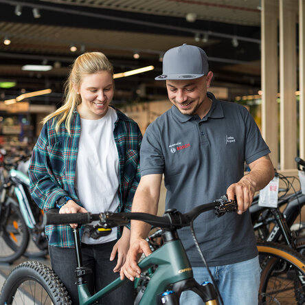 Ein Bosch eBike Experte erklärt einer lächelnden Kundin in einem Fahrradgeschäft die Einstellungen des eBikes.