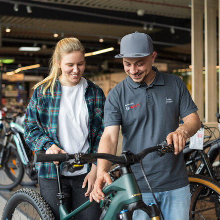 Un esperto di eBike Bosch spiega le impostazioni della eBike a un cliente sorridente in un negozio di biciclette.