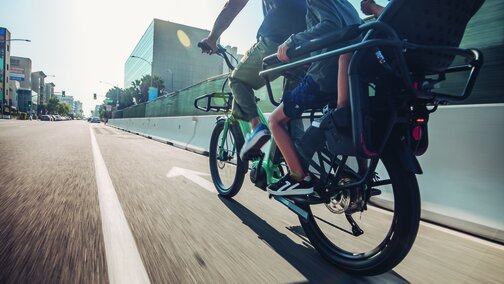 An eBiker is riding quickly on a road, with two children riding behind him on the eBike.