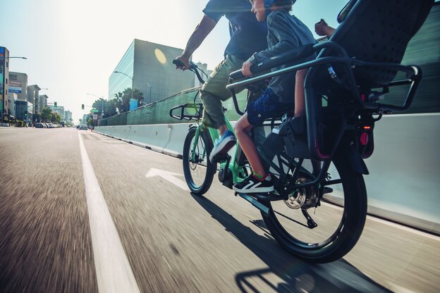 An eBiker is riding quickly on a road, with two children riding behind him on the eBike.