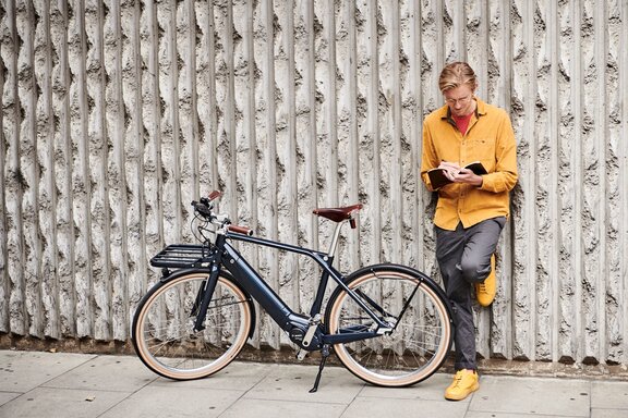 Architekt Edward Crooks opiera się o strukturę betonową, obok niego stoi jego czarne eBike.