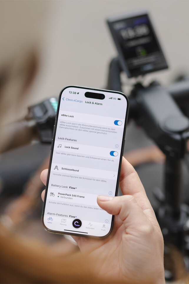Blick über die Schulter einer Person, die ein Smartphone hält und in der eBike Flow App Einstellungen zu eBike Lock und Alarm vornimmt.