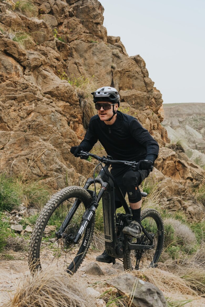 Ein Mountainbiker in voller Montur fährt mit seinem eMTB einen technisch anspruchsvollen Trail in einer felsigen, kargen Gebirgslandschaft.
