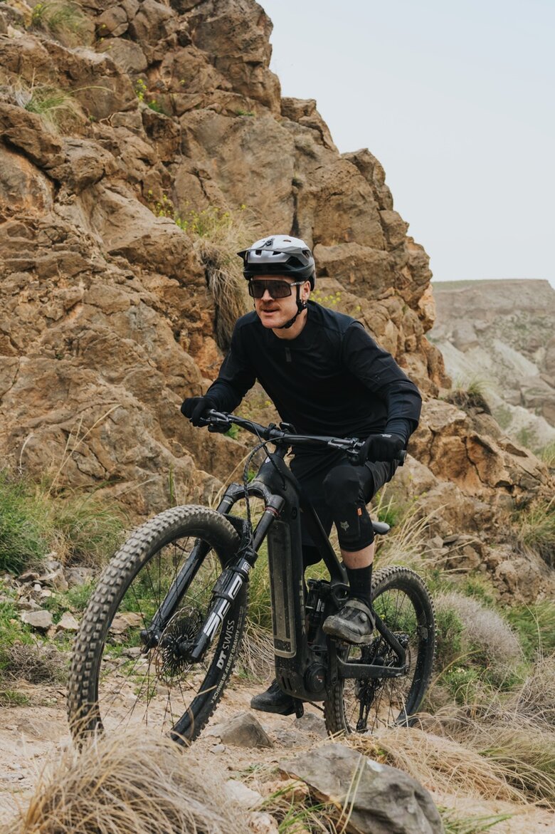 Ein Mountainbiker in voller Montur fährt mit seinem eMTB einen technisch anspruchsvollen Trail in einer felsigen, kargen Gebirgslandschaft.