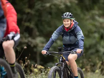A woman is riding an eBike and smiling. Blurred trees can be seen in the background.