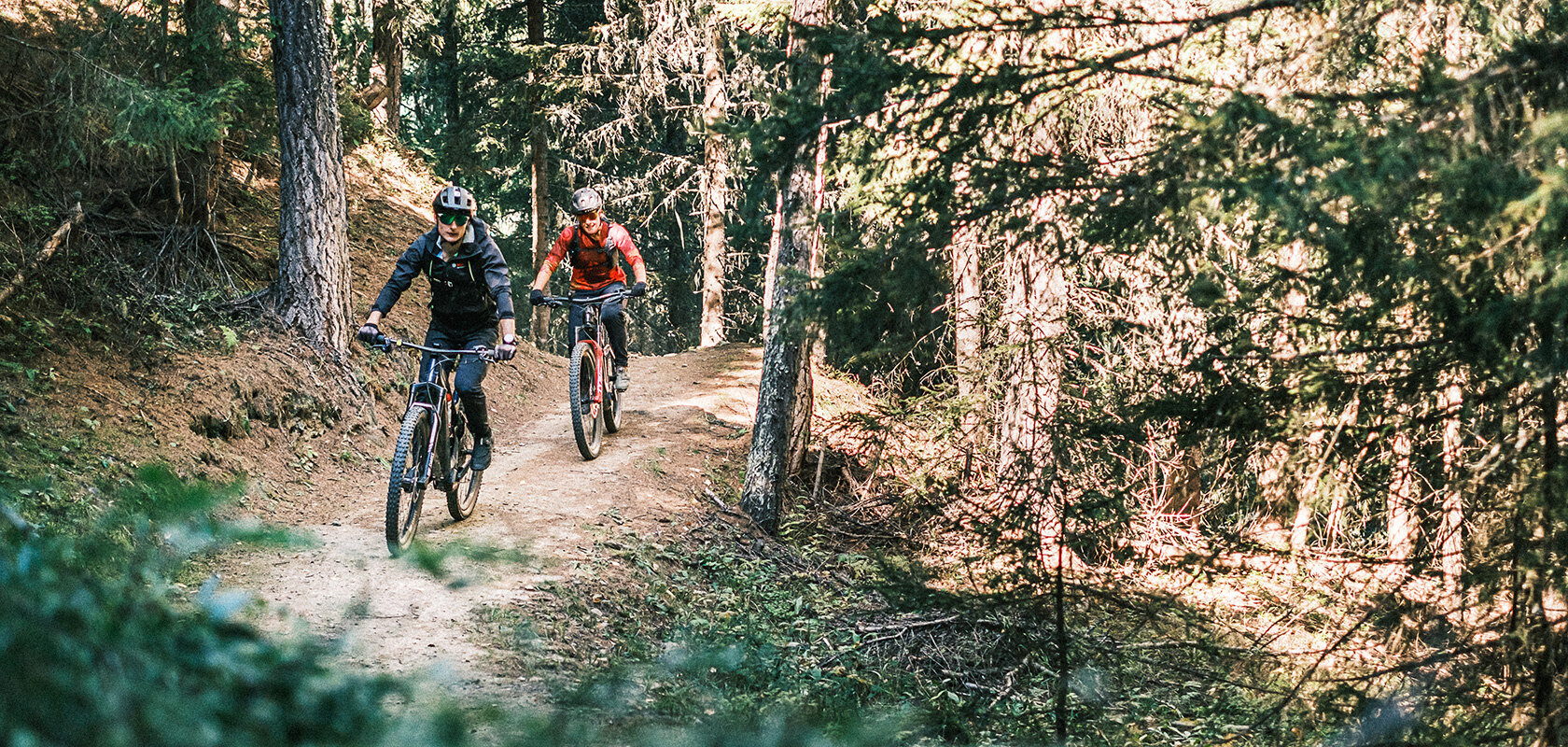 Deux conducteurs de VTT à assistance électrique descendent l’un après l’autre un chemin forestier.