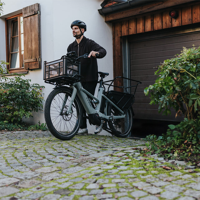 Ein Mann mit Helm schiebt sein eCargo Bike aus einer Garage.