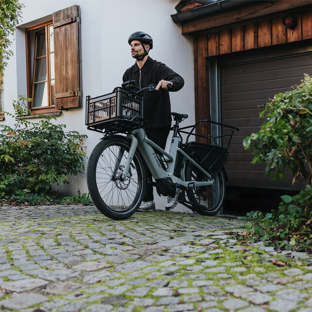 Ein Mann mit Helm schiebt sein eCargo Bike aus einer Garage.