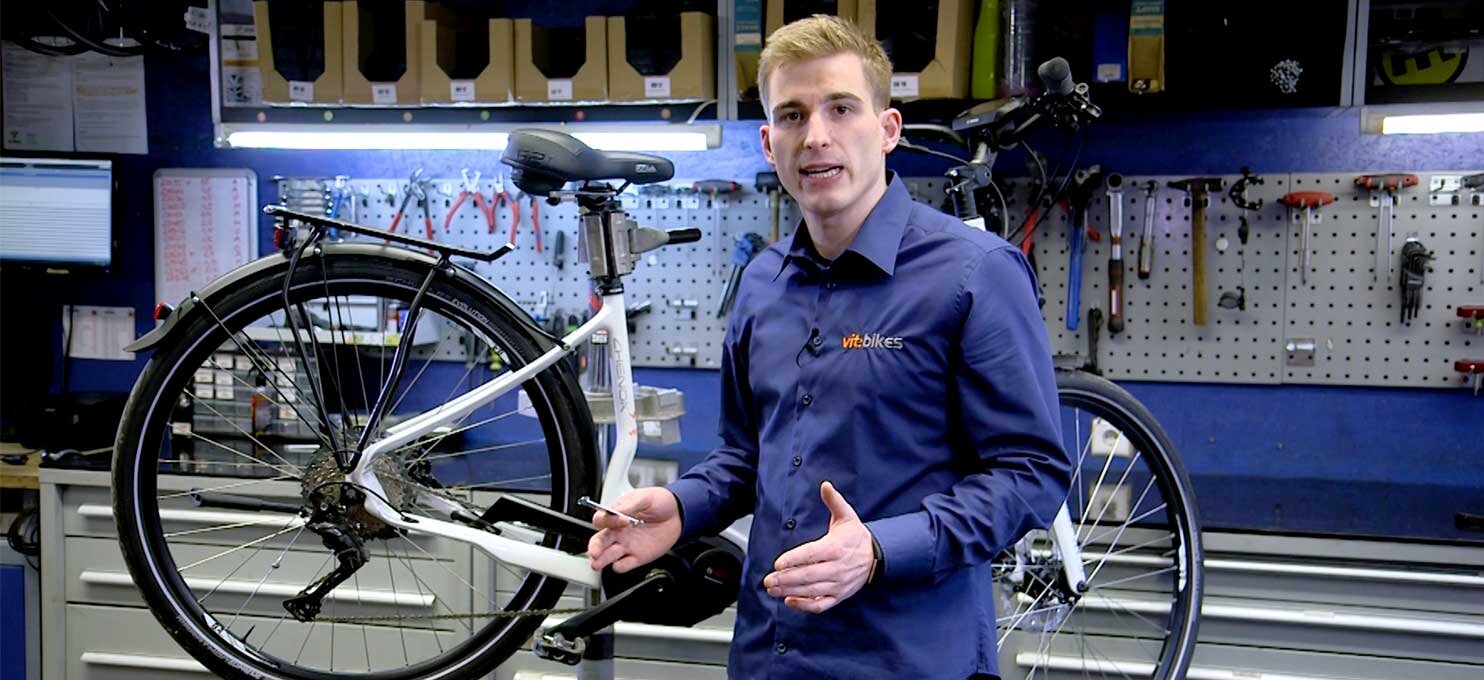 A Bosch technician stands in a bicycle workshop in front of an eBike, explaining something.