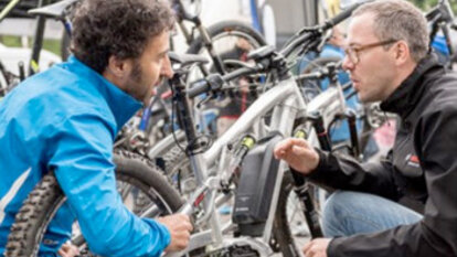A Bosch eBike employee and a man are kneeling in front of an eBike while the employee explains something.
