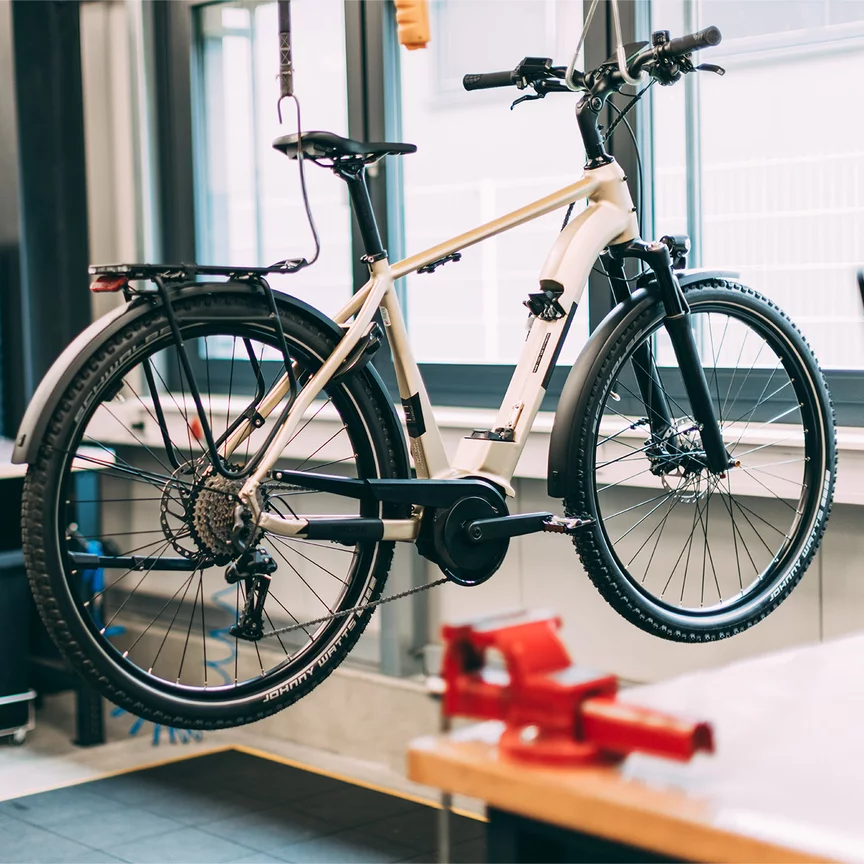 An eBike is suspended above the ground in a workshop. In the background, a Bosch employee is visible.