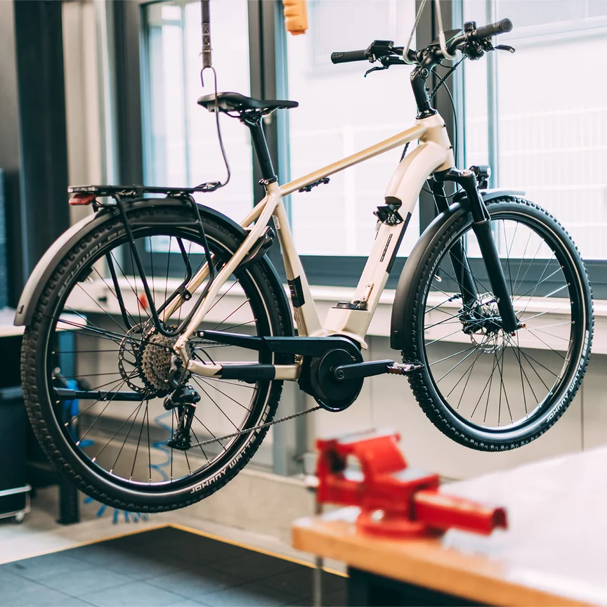 Ein eBike hängt über dem Boden in einer Werkstatt. Im Hintergrund sieht man einen Bosch Mitarbeiter.