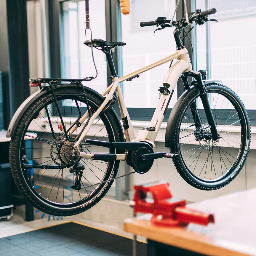 Ein eBike hängt über dem Boden in einer Werkstatt. Im Hintergrund sieht man einen Bosch Mitarbeiter.