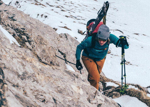 Une femme pratiquant le ski de randonnée, avec des montagnes enneigées en arrière-plan.