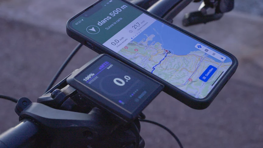 Gros plan d’un écran Kiox et d’un smartphone fixé à côté sur le guidon d’un vélo électrique.