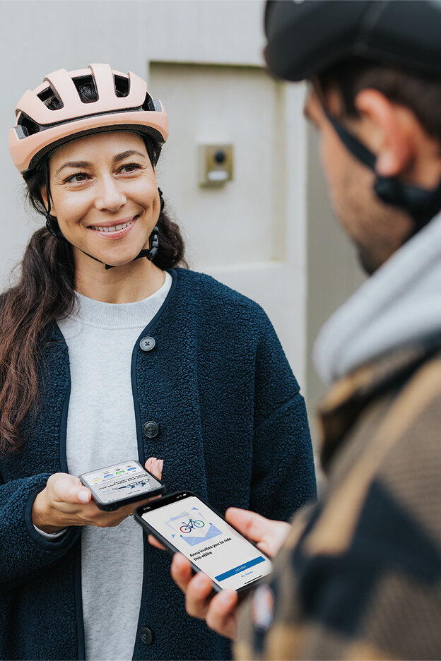 En kvinna och en man står leende mittemot varandra och kopplar ihop sina smartphones i eBike Flow-app. Båda har cykelhjälm.