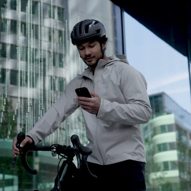 Een man met een helm staat bij zijn eBike en kijkt op zijn smartphone.