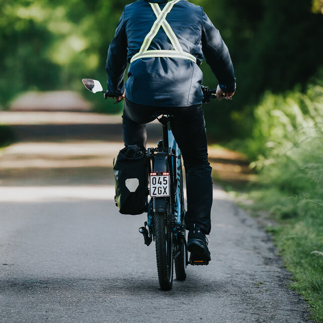 eBike rider travels on a narrow road in nature with light reflectors on his back.