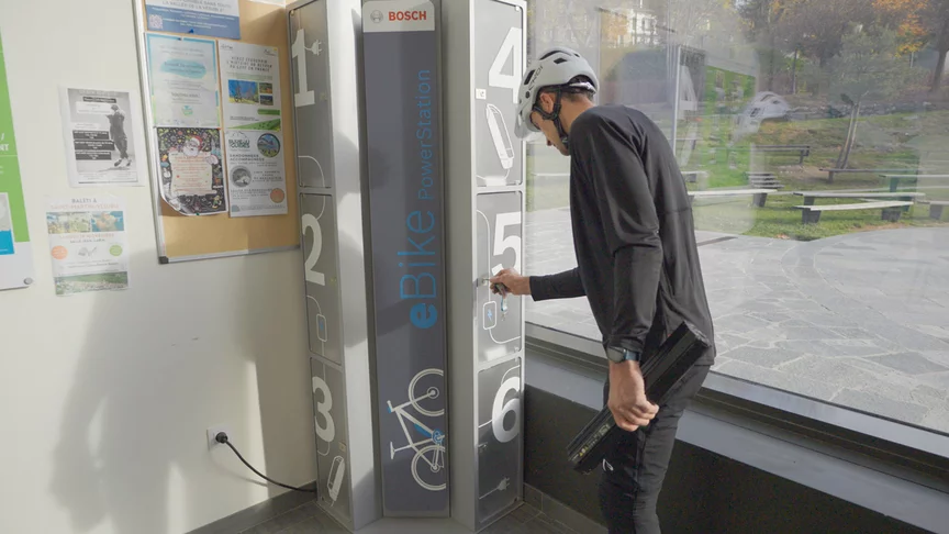 Un homme se tient devant une Bosch VAE PowerStation et tient une clé dans une main et une batterie pour VAE Bosch dans l’autre.