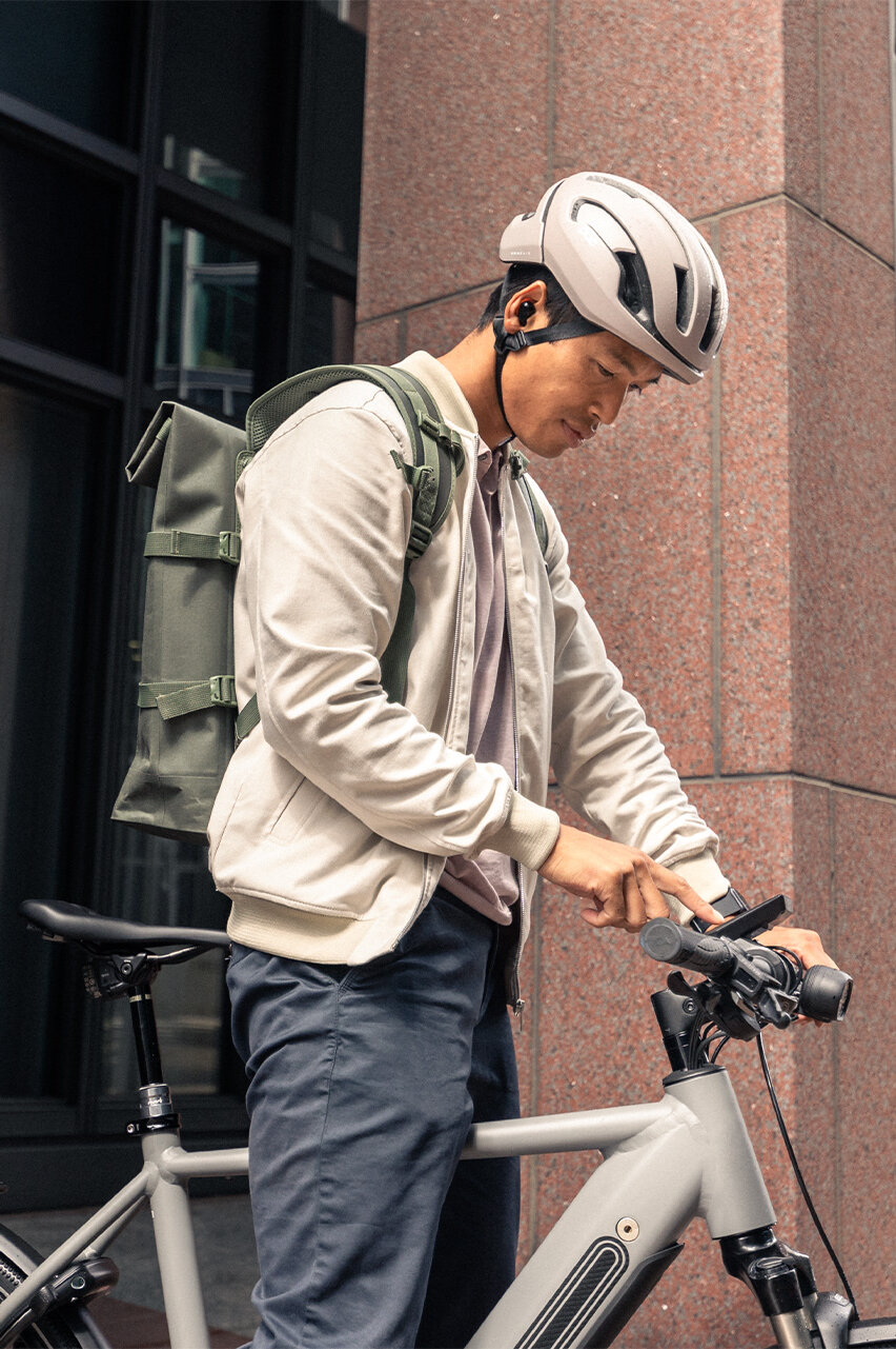 A man in an urban setting firmly grips the handlebars of his eBike and taps on the smartphone attached to the eBike.
