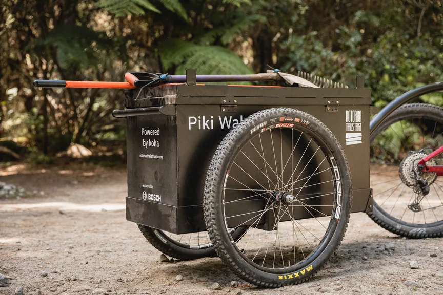 Close-up of the cargo basket on an eCargo bike, where a shovel and rake are resting. The cargo basket displays the words: 'Powered by koha', 'Rotoria Trails Trust', and the Bosch logo.
