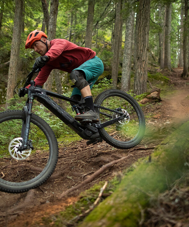A man is riding an eBike on a challenging mountain bike trail through the forest, surrounded by dense trees.