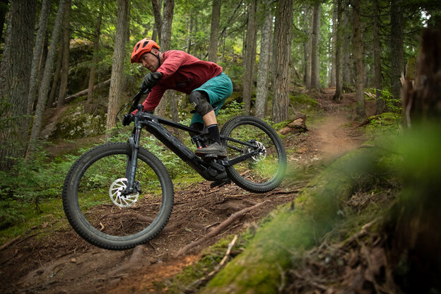 A man is riding an eBike on a challenging mountain bike trail through the forest, surrounded by dense trees.