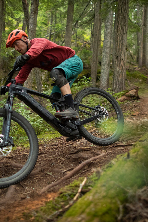 Un homme parcourt un sentier de VTT difficile à travers la forêt sur un VTT électrique, entouré d'arbres denses.